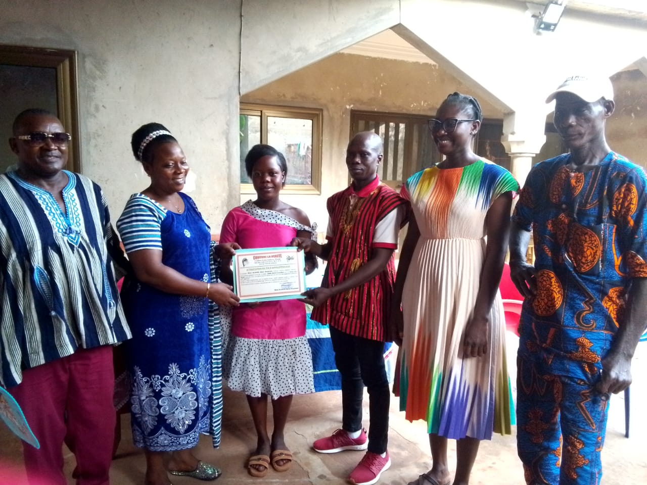 Remise d'une attestation de fin d'apprentissage à une jeune fille, entourée de sa famille
